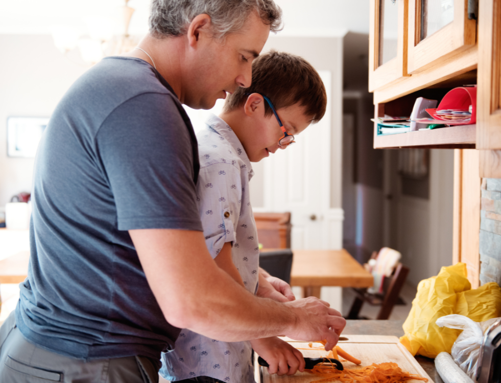 A young adult being assisted by a caregiver in a kitchen, preparing a meal together at Concept Care Community Services.