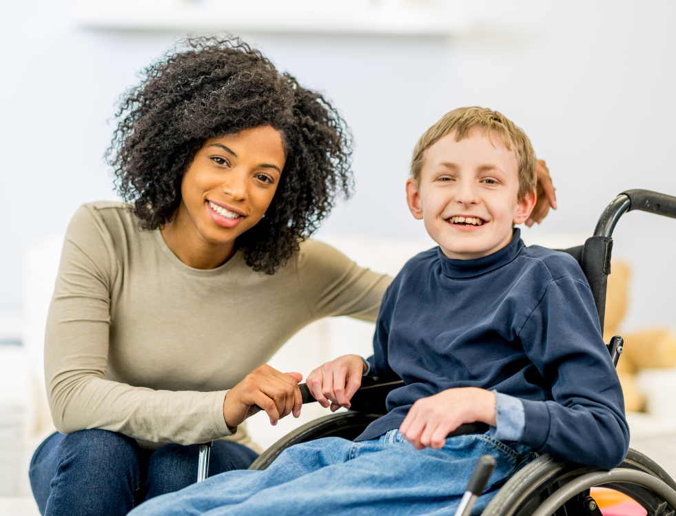 A smiling caregiver sitting beside a child in a wheelchair, representing the supportive environment in learning disability services.