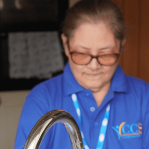 A caregiver from Concept Care Community Services wearing a blue uniform and glasses, smiling while attending to a task.