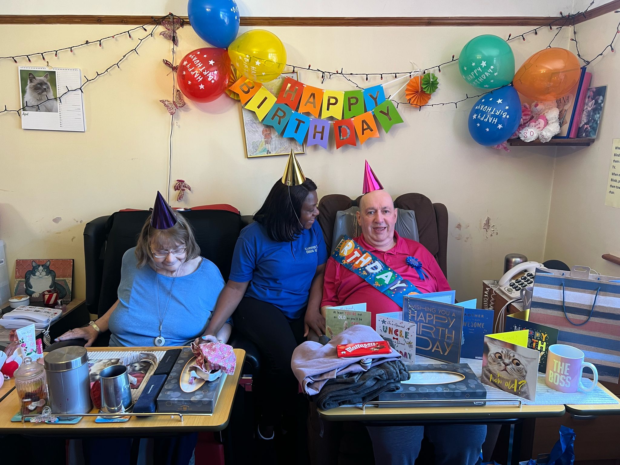 A birthday celebration for a client with party hats, balloons, and a carer, surrounded by birthday cards and decorations.