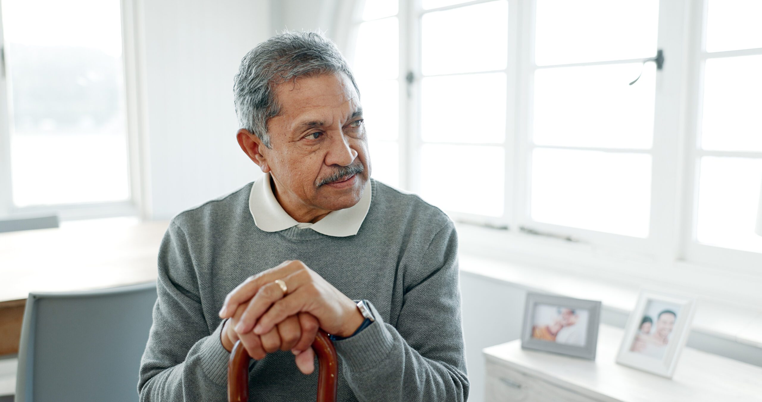 Senior Indian man sitting at home with walking stick, looking thoughtful