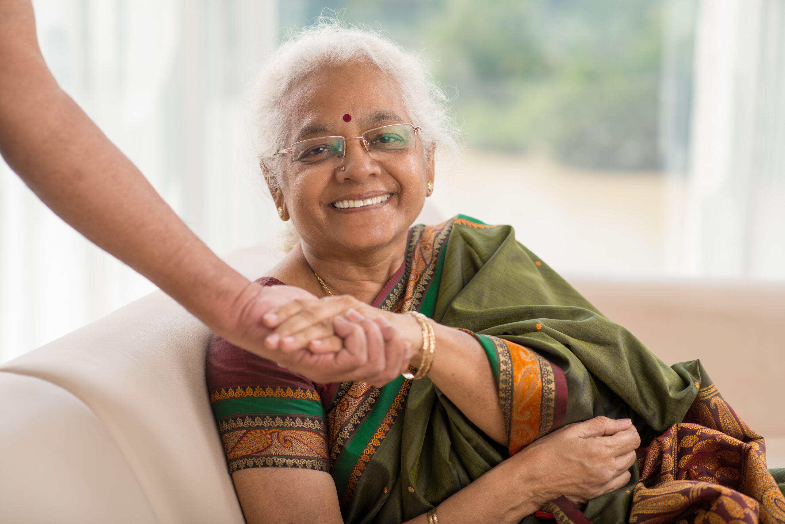 Elderly Indian woman smiling and holding her spouse’s hand at home